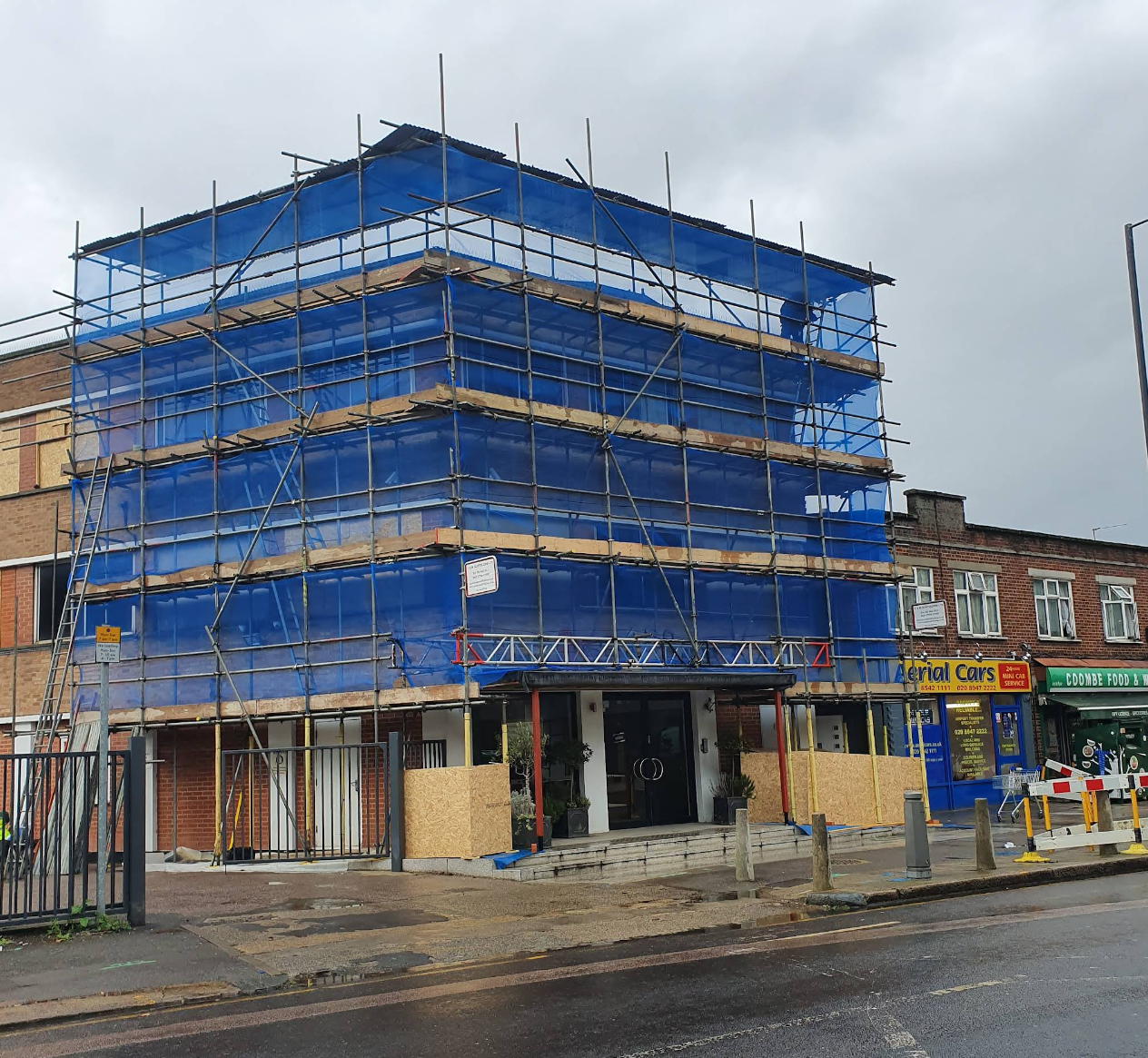 Commercial building with full blue scaffolding sheeting and tube-and-fitting rig